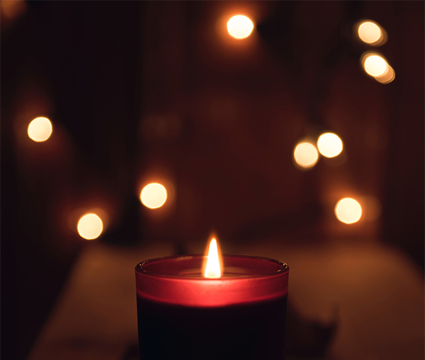 Lit candle with fairy lights in background